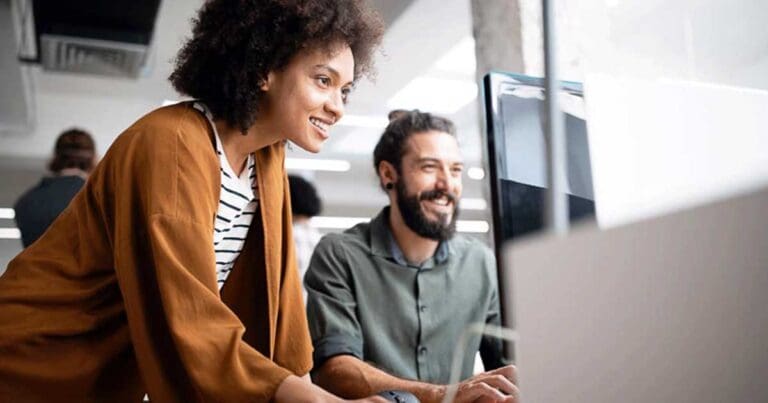 man and woman standing at a computer smiling