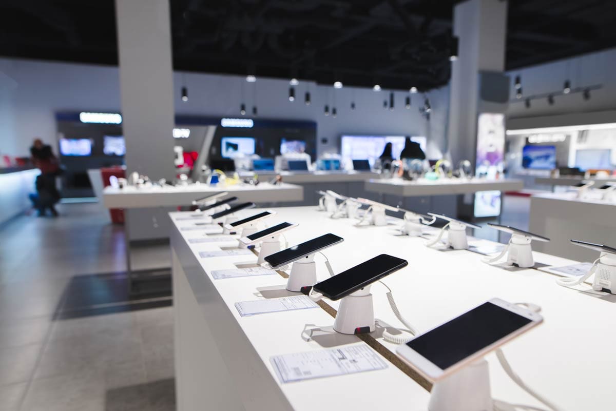 Smartphones and devices displayed on table in an electronics retailer store.