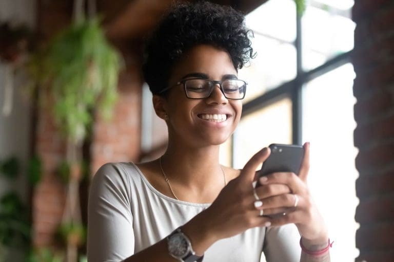 Smiling African American woman using phone, browsing mobile apps or websites