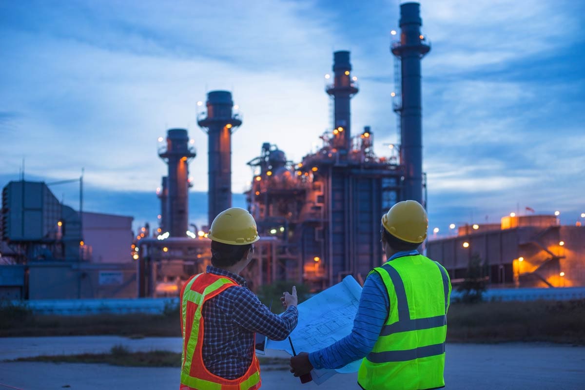 Two industrial engineers in hard hats and safety vests reviewing strategy at an energy plant